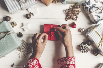 Wall Mural - merry christmas and happy new year flat lay. hands wrapping red present gift box on rustic white wood with presents and ornaments, top view. seasonal greetings. happy holidays, modern xmas card