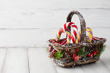 Wall Mural - Christmas wicker basket with striped candy canes on white wooden table, festive decoration