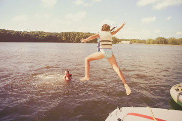 Kids jumping off a boat into the lake. Vintage film effect, noise and color fringing, dark edges