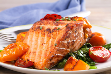 Salmon fillet with spinach and tomatoes on white plate on rustic wooden background