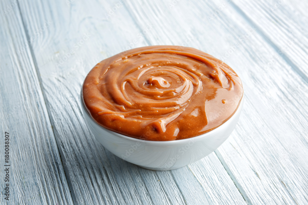Bowl with tasty caramel sauce on wooden table