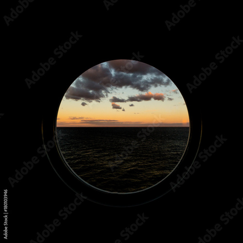 Fotografie, Obraz view through porthole on dawn at sea with clouds