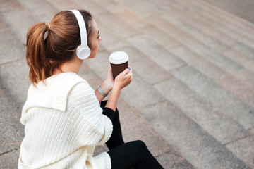 Wall Mural - Young amazing woman sitting on steps drinking coffee. Looking aside.