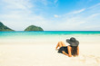 Vacation concept: woman in black hat on beautiful beach looking on island in blue water.