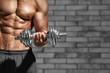 © Africa Studio - Muscular young man with dumbbell against brick wall