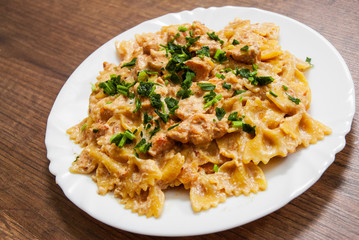 Wall Mural - Sliced fried chicken fillet in a creamy sauce. with farfalle pasta. in plate on a wooden background