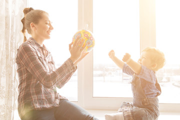 Happy mother and her baby playing colorful ball at home over window