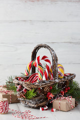 Wall Mural - Christmas wicker basket with striped candy canes and gifts on white wooden table, festive decoration