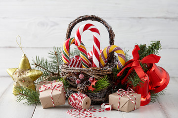 Wall Mural - Christmas wicker basket with striped candy canes and wrapped gifts on white wooden table, festive decoration