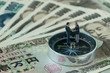 © Nuthawut - miniature figure businessmen handshaking and standing on compass on pile of japanese yen banknotes as financial leader direction or agreement concept