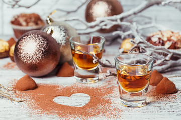 Whiskey or liqueur, truffle chocolate candies in cocoa powder and christmas decorations on white wooden background.