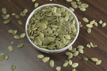 Wall Mural - Vegan food. Raw pumpkin seeds for roasting in a white dish. Wooden background.