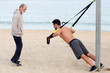 © Adam Gregor - Athletic man making suspension training exercise on the beach with coach