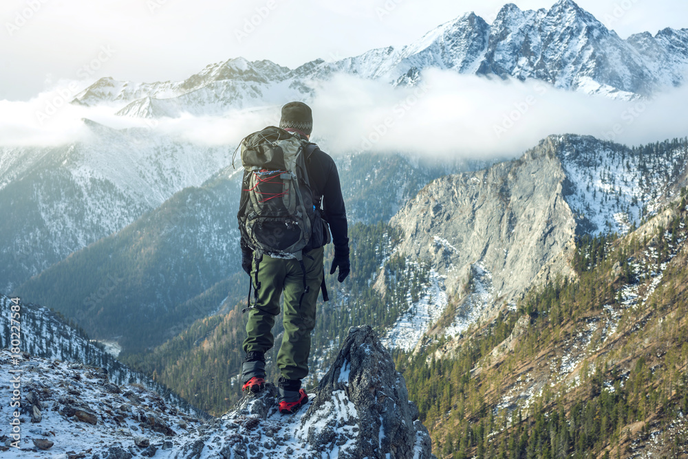 Man hiker with backpack on top of the mountain back, looking at the snow slope. Concept motivation and goal achievement - obrazy, fototapety, plakaty 