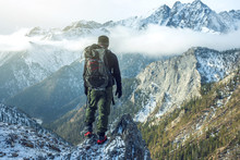 Man Hiker With Backpack On Top Of The Mountain Back, Looking At The Snow Slope. Concept Motivation And Goal Achievement