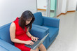 © reewungjunerr - Business girl in red dress sit on sofa for work on laptop,business woman work in office concept