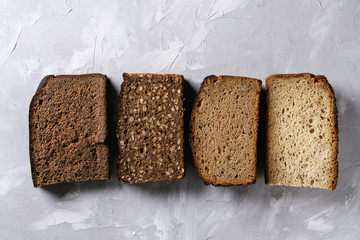 Variety loaves of sliced homemade rye bread whole grain and seeds over gray texture background. Top view, copy space. Healthy eating