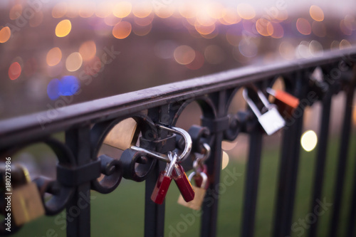 Fotografie, Obraz Padlock pinned to the rail of the iron bridge with nice, fuzzy city lights in th