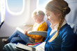 © MNStudio - Adorable little children traveling by an airplane. Girl sitting by aircraft window and reading her ebook during the flight.