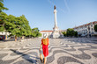 Young woman tourist walking on the Rossio square with Pedro statue during the morning light in Lisbon city, Portugal