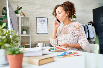 Portrait of pretty mixed race woman speaking by phone discussing color palette for interior design, holding color swatches