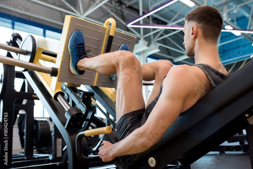 Plakat Tylni widok robi noga mięśniowi sportowiec ćwiczy używać maszynę w nowożytnym gym