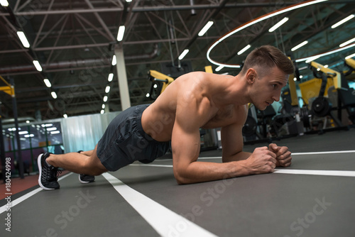 Zdjęcie XXL Portret młody mięśniowy mężczyzna z nagą klatką piersiową robi deski ćwiczeniu na podłoga podczas treningu w nowożytnym gym