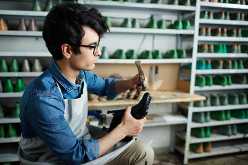 Wall Mural - Young shoe master with hammer repairing footwear or making new pair of shoes