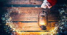 Christmas Scene. Santa Claus Hand Holding Vintage Oil Lamp Over Holiday Wooden Background