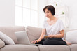 © Prostock-studio - Pensive girl with laptop and mobile sitting on beige couch