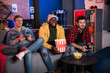© Yakobchuk Olena - Back to childhood. Cheerful young men are sitting on sofa and expressing gladness. African guy is sitting with popcorn while his friends enjoying play station. They are looking at screen with smile