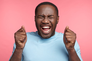 Wall Mural - Lucky happy overjoyed dark skinned male winner clenches fists, rejoices triumph at work, glad to recieve high profits, has own prosperous business. Attractive African American man achieves goals