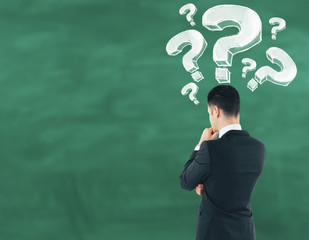 Poster - businessman on chalkboard background looking at drawn question marks