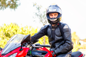 Handsome rider guy in black leather biker jacket and helmet sit on classic style racer motorbike