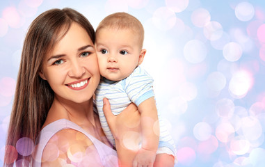 Poster - Portrait of happy young woman with cute baby on blurred lights background