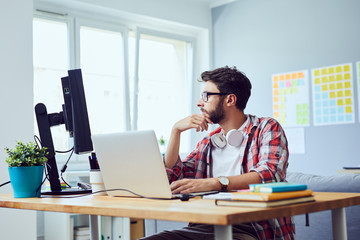 Side view of young web developer looking at screen and thinking about work project