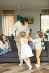 Wall Mural - Young father playing with son and daughter at home, happy husband dad enjoys spending time with kids while wife mother sitting on sofa, little children love their daddy having fun together, vertical