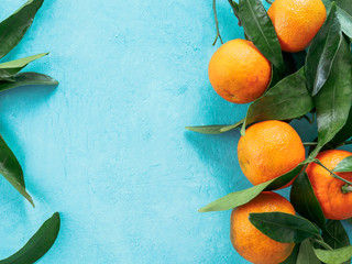 Wall Mural - Tangerines, oranges, mandarins, clementines, citrus fruits with leaves on blue concrete background. Top view or flat-lay. Copy space.