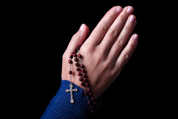 Female hands praying holding a rosary with Jesus Christ in the cross or Crucifix on black background. Woman with Christian Catholic religious faith