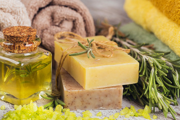 Natural cosmetic oil and natural handmade soap with rosemary on rustic wooden background.