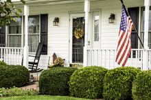 White Colonial Home Decorated For Fall With American Flag Flying From The Front Porch With Rocking Chairs
