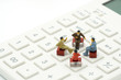 Miniature 4 people sitting on red staples placed on a white calculator. meeting or Discussion as background business concept with copy space.