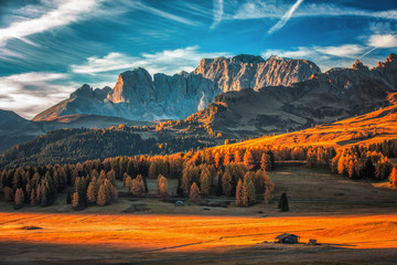 Aerial autumn sunrise scenery with yellow larches and small alpine building and Odle - Geisler mountain group on background. Alpe di Siusi (Seiser Alm), Dolomite Alps, Italy