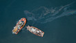 Fishing boats on the ocean releasing fuel to the environment and polluting the nearby ocean with the oil spill