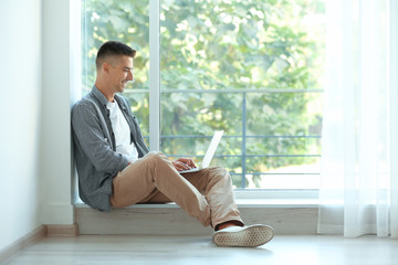 Canvas Print - Young man using laptop near window at home