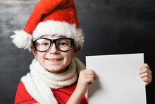 Small Boy In Red Shirt And White Knitted Scarf Holding A White Sheet Of Paper With Text "Dear Santa'