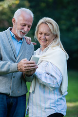 Wall Mural - Happy senior couple using a phone, outdoors 