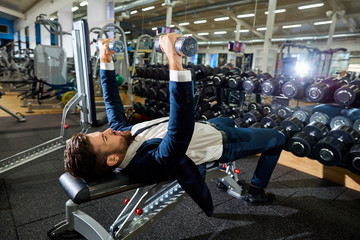 Businessman doing exercises with dumbbells in the gym.