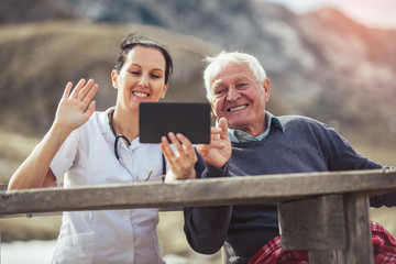 Canvas Print - Smiling caregiver nurse and  disabled senior patient using digital tablet outdoor