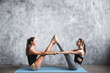 Two attractive sport girls workout asana boat yoga pose on mat on gray stylish background.